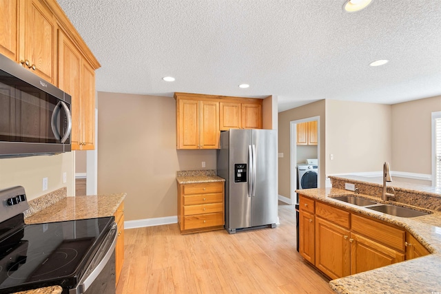 kitchen with a sink, light stone counters, light wood-type flooring, and stainless steel appliances