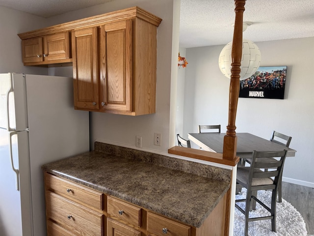 kitchen with brown cabinetry, wood finished floors, freestanding refrigerator, and dark countertops