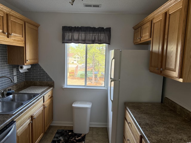 kitchen featuring dark countertops, visible vents, decorative backsplash, dishwasher, and a sink