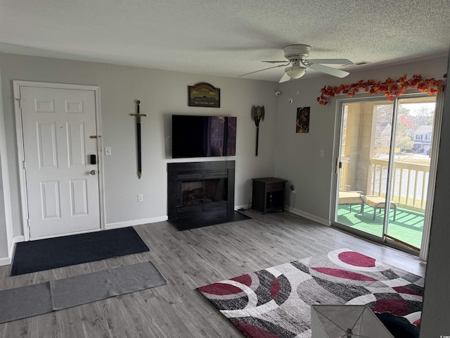 living area with baseboards, a ceiling fan, wood finished floors, and a textured ceiling