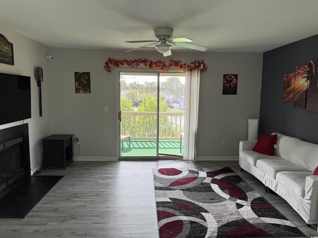 living room with baseboards, a textured ceiling, wood finished floors, and ceiling fan