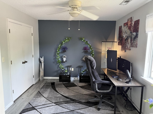 home office with a textured ceiling, wood finished floors, ceiling fan, and visible vents