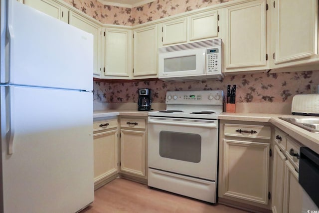 kitchen with light countertops, light wood-style flooring, cream cabinetry, and white appliances