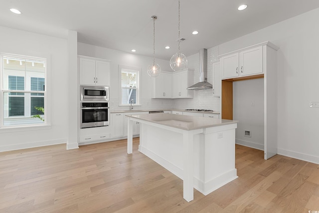 kitchen featuring appliances with stainless steel finishes, wall chimney range hood, a sink, backsplash, and light countertops
