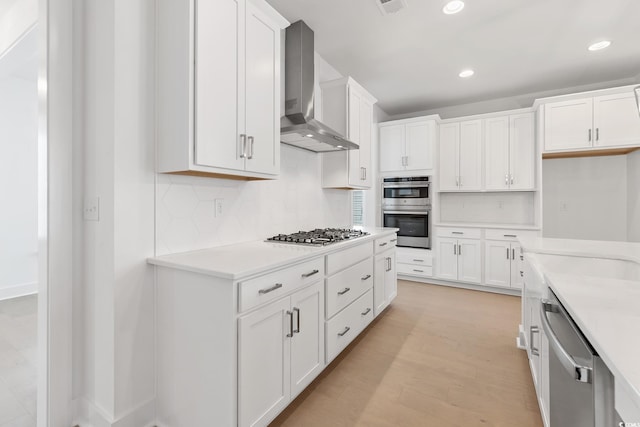 kitchen with wall chimney range hood, appliances with stainless steel finishes, tasteful backsplash, white cabinetry, and light countertops