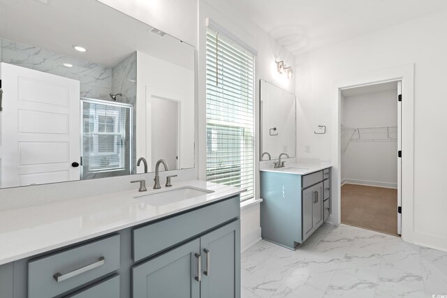 full bath with a stall shower, marble finish flooring, two vanities, a walk in closet, and baseboards