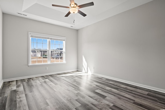 unfurnished room with a tray ceiling, wood finished floors, ceiling fan, and baseboards