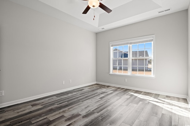 spare room featuring a raised ceiling, wood finished floors, ceiling fan, and baseboards