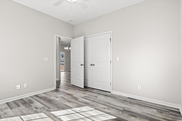 unfurnished bedroom featuring wood finished floors, a closet, baseboards, and a chandelier