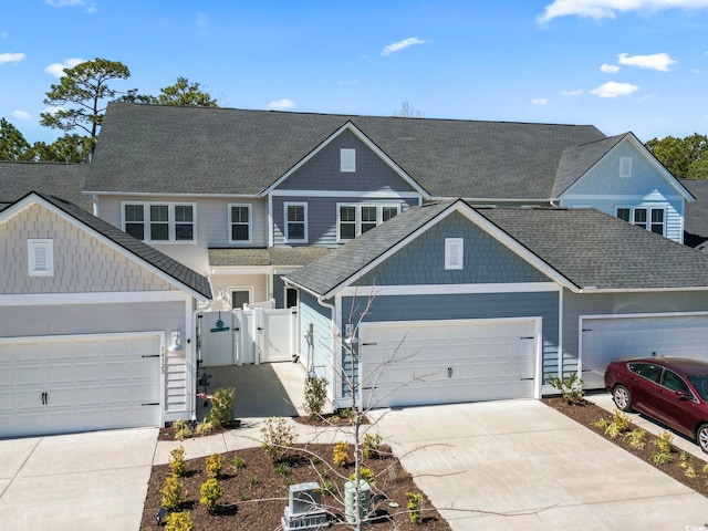 view of front facade featuring roof with shingles, a gate, driveway, an attached garage, and fence