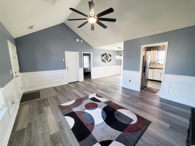living room featuring a ceiling fan, wainscoting, wood finished floors, a decorative wall, and lofted ceiling