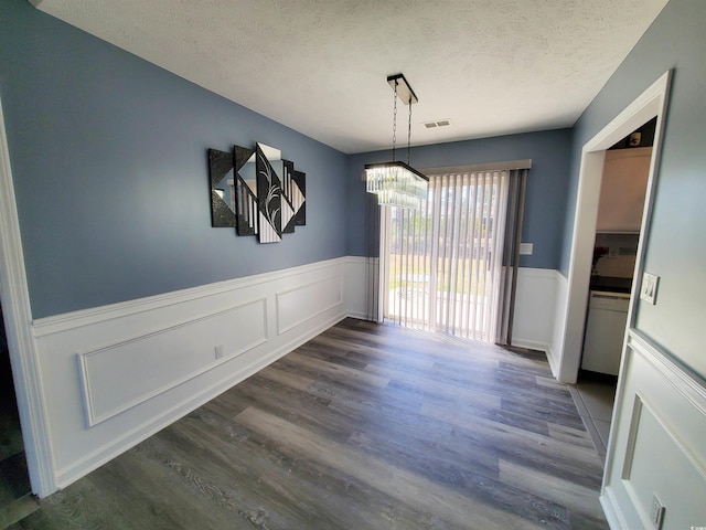 unfurnished dining area with a chandelier, a textured ceiling, a wainscoted wall, dark wood finished floors, and a decorative wall