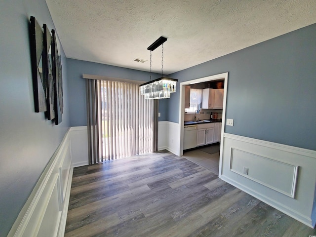 unfurnished dining area featuring a chandelier, wainscoting, plenty of natural light, a textured ceiling, and dark wood-type flooring