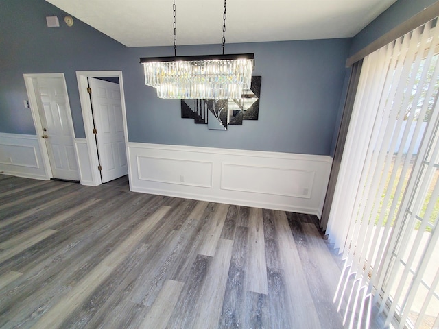 unfurnished dining area featuring a chandelier, wood finished floors, wainscoting, and a decorative wall