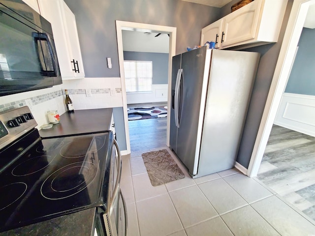 kitchen featuring stainless steel appliances, white cabinetry, wainscoting, and light tile patterned floors