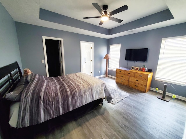 bedroom with a raised ceiling, baseboards, wood finished floors, and a ceiling fan