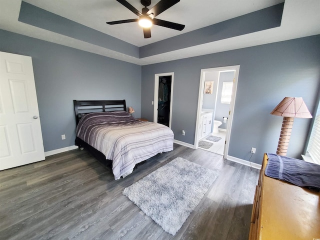 bedroom featuring a raised ceiling, baseboards, wood finished floors, and ensuite bath