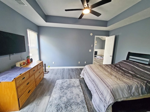 bedroom featuring wood finished floors, a raised ceiling, a ceiling fan, and baseboards