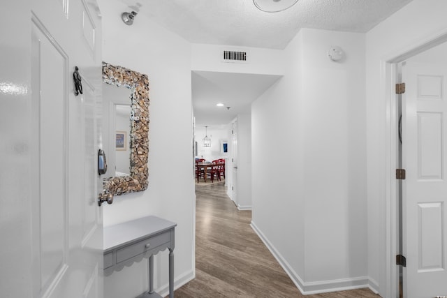corridor with baseboards, a textured ceiling, visible vents, and wood finished floors