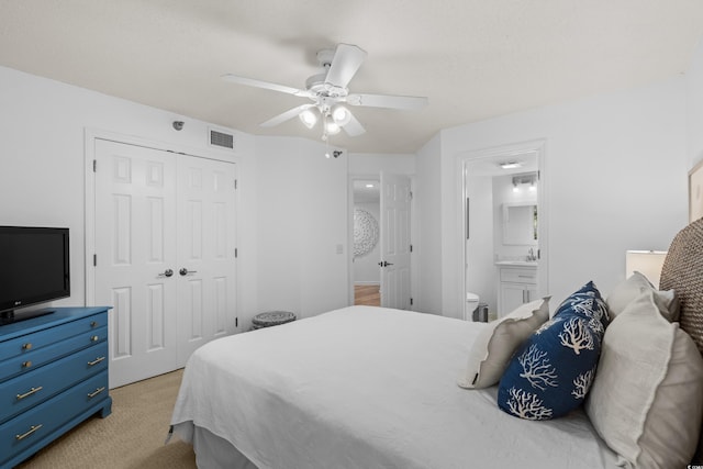 bedroom with a closet, visible vents, light carpet, ensuite bathroom, and a ceiling fan