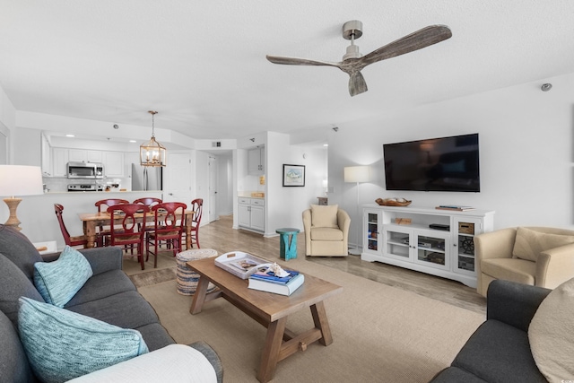 living area with light wood-type flooring and ceiling fan with notable chandelier