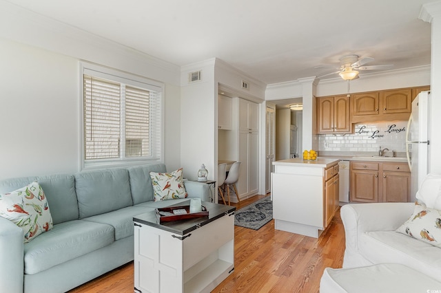 living room with crown molding, light wood-style floors, ceiling fan, and visible vents
