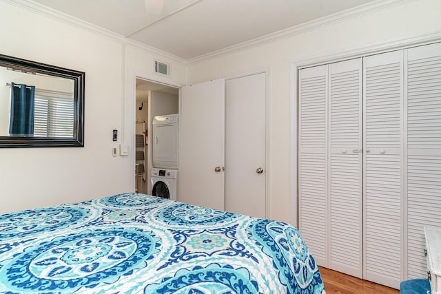 bedroom featuring crown molding, light wood-type flooring, stacked washer and dryer, visible vents, and a closet