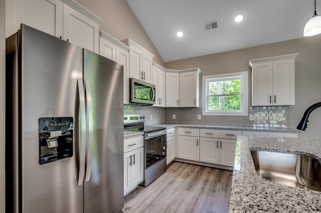 kitchen with appliances with stainless steel finishes, a sink, vaulted ceiling, white cabinets, and tasteful backsplash