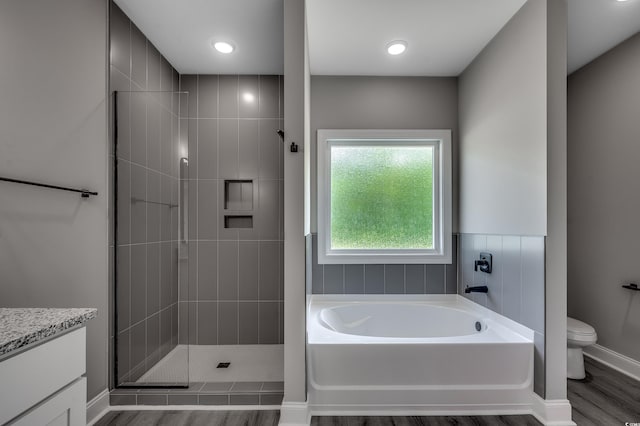 bathroom featuring a garden tub, a tile shower, wood finished floors, toilet, and vanity