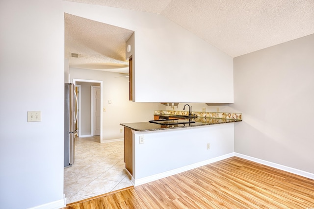 1161 Ganton Way, Myrtle Beach, SC 29588 - kitchen with freestanding refrigerator, a textured ceiling, dark countertops, a peninsula, and vaulted ceiling