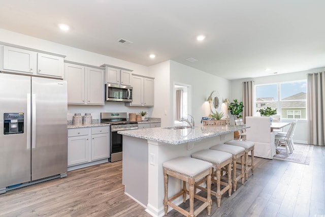 kitchen with a breakfast bar, a sink, stainless steel appliances, light wood-type flooring, and visible vents