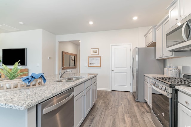 kitchen with wood finished floors, a center island with sink, light stone counters, a sink, and stainless steel appliances