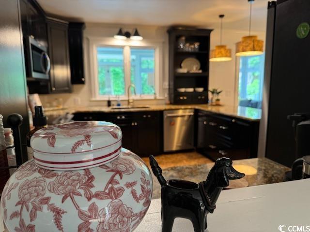 kitchen featuring stainless steel appliances, a sink, dark cabinetry, hanging light fixtures, and open shelves