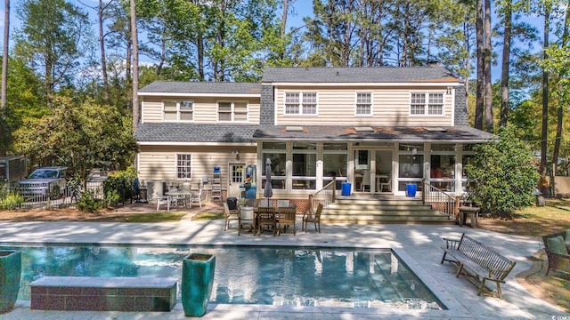 rear view of house with a sunroom, a pool with connected hot tub, a patio, fence, and outdoor dining area