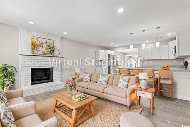 living area with wood tiled floors, recessed lighting, and a brick fireplace