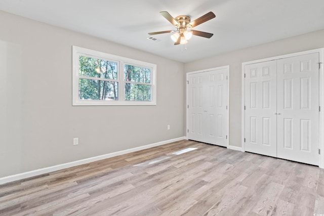 unfurnished bedroom with multiple closets, light wood-style flooring, baseboards, and ceiling fan