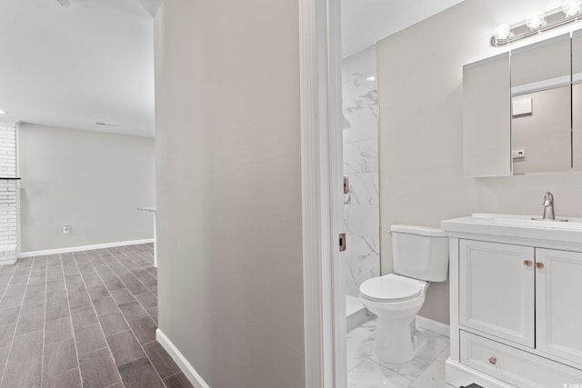 bathroom with baseboards, toilet, a walk in shower, vanity, and wood finished floors