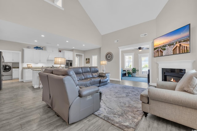 1109 Bonnet Dr, North Myrtle Beach, SC 29582 - living room with high vaulted ceiling, washer / dryer, a glass covered fireplace, ceiling fan, and light wood-type flooring
