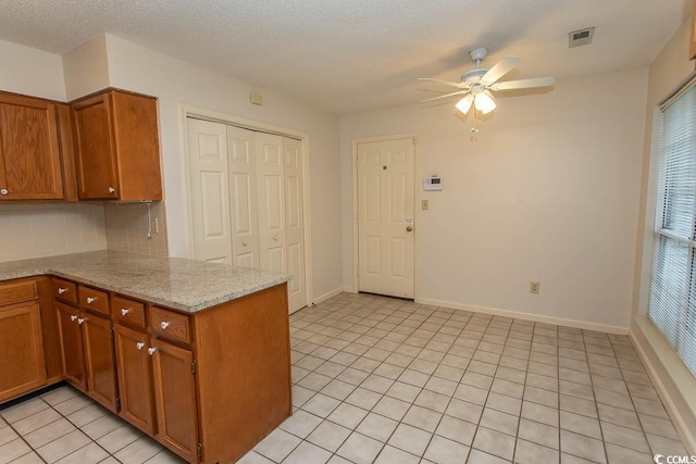1001 Cardinal Ct, Murrells Inlet, SC 29576 - kitchen with ceiling fan, brown cabinetry, backsplash, light tile patterned floors, and a peninsula