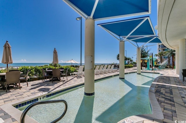 community pool with a patio, outdoor dining space, and a water view