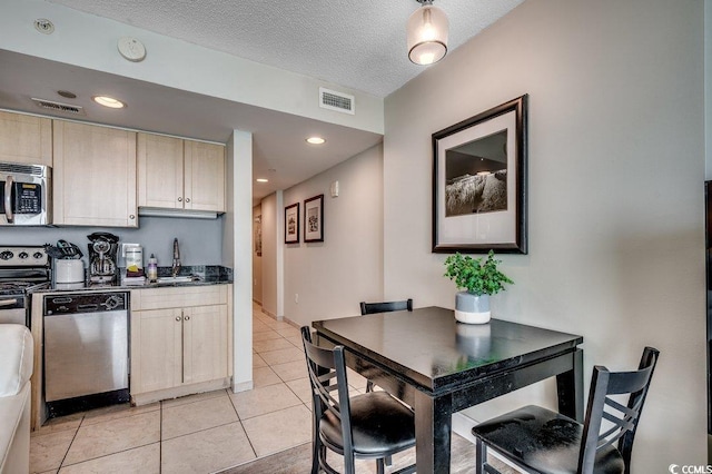 kitchen with appliances with stainless steel finishes, dark countertops, a sink, light tile patterned floors, and a textured ceiling