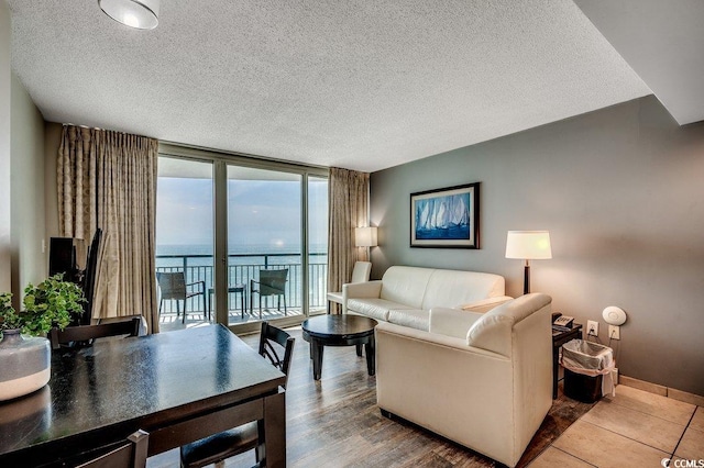 living room with expansive windows, a textured ceiling, a water view, and baseboards