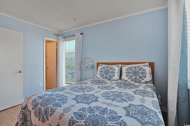 bedroom featuring crown molding, a textured ceiling, wood finished floors, and visible vents