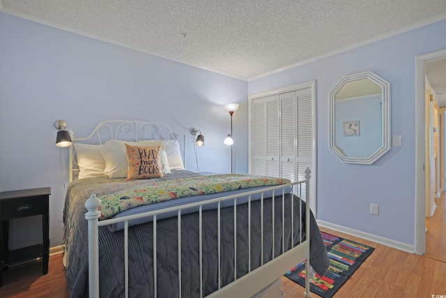 bedroom with a closet, ornamental molding, wood finished floors, baseboards, and a textured ceiling