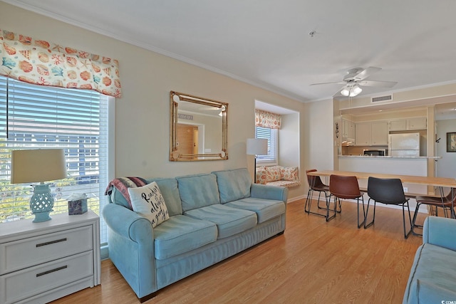 living area with visible vents, a ceiling fan, light wood finished floors, and crown molding
