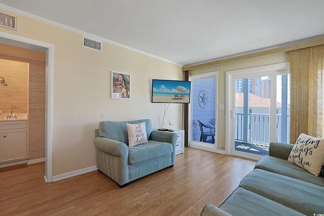 living area featuring baseboards, visible vents, ornamental molding, and wood finished floors