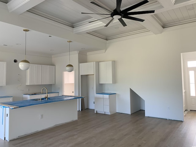 kitchen with ornamental molding, white cabinets, light wood-style floors, a kitchen island with sink, and beam ceiling