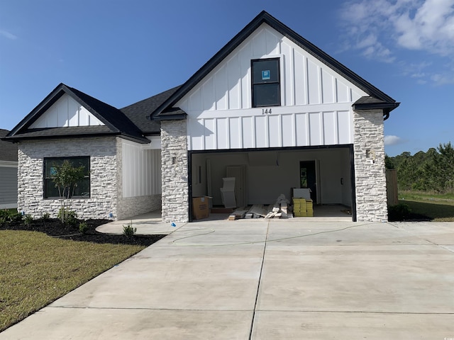 modern farmhouse featuring concrete driveway, board and batten siding, stone siding, and a front yard