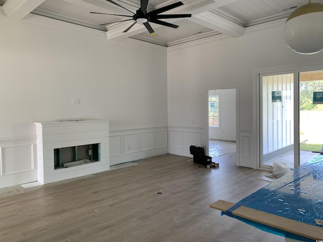 unfurnished living room featuring crown molding, a glass covered fireplace, beam ceiling, and coffered ceiling
