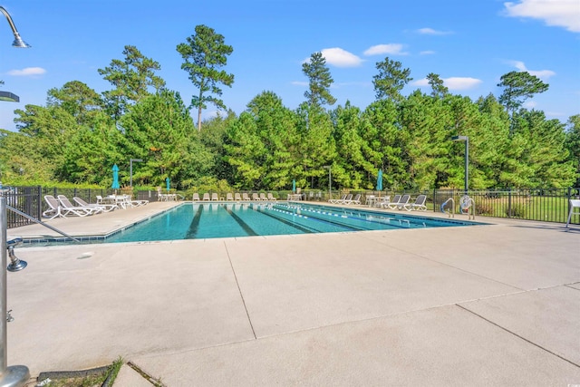 community pool featuring a patio area, fence, and view of wooded area